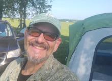 Man smiling near a tent and car in a sunny field.