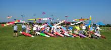 Group with colorful model planes on a grassy field, clear sky overhead.