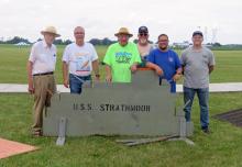 Five men standing behind a USS Strathmoor sign on a grassy field.