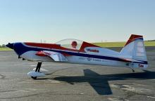 A small, aerobatic airplane with Futaba branding on a tarmac under a clear sky.